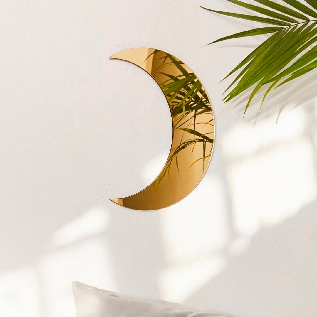 Gold crescent mirror with green leaves on a white background
