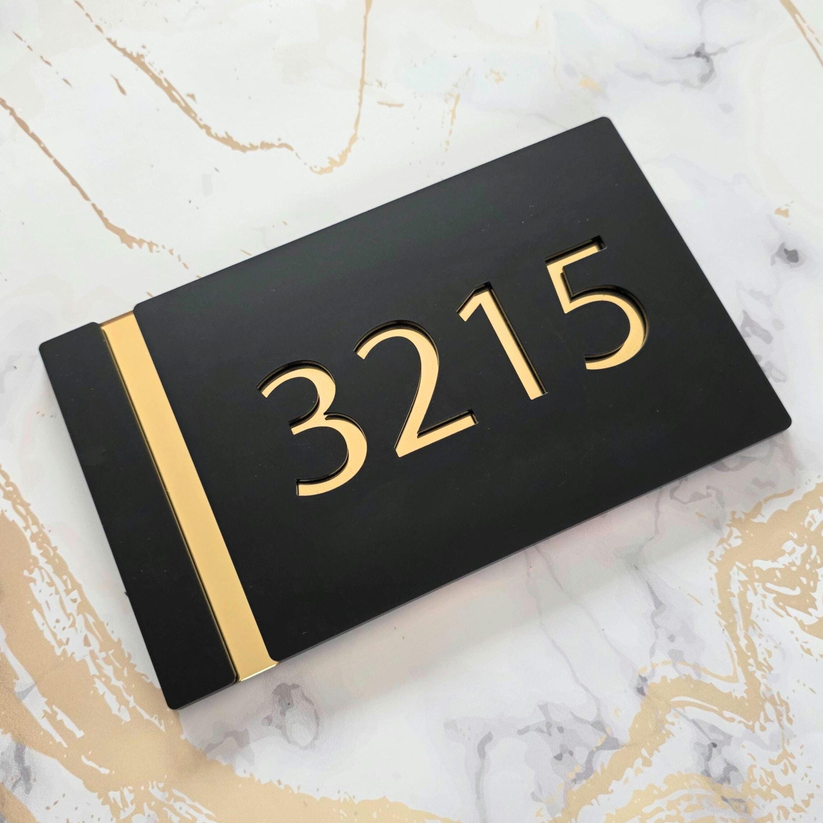 A black rectangular house number sign with a gold stripe. The number 3215 is cut out of the sign and is gold in color.