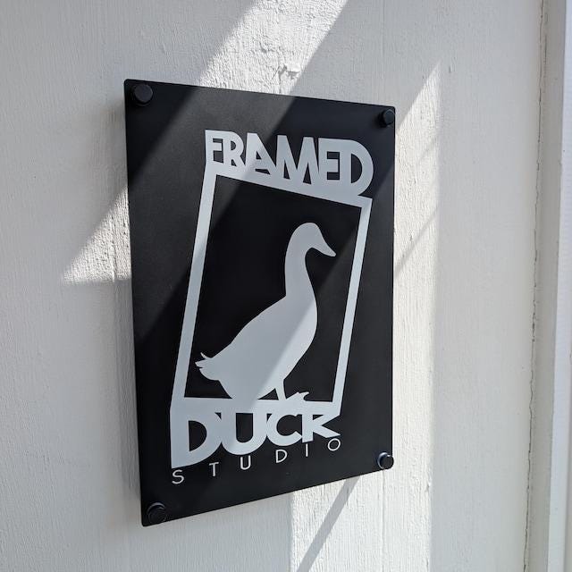 matte black custom acrylic business logo sign, printed with white UV ink. Mounted to the wall of a studio entrace with black standoff fixings.